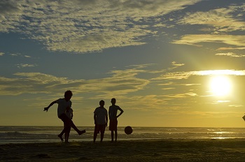 Foto van volwassenen die vlak voor zonsondergang gezellig een balletje trappen op het strand
